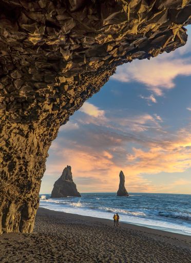 A young couple walking on a sandy Reynisfjara Beach at sunset in Iceland