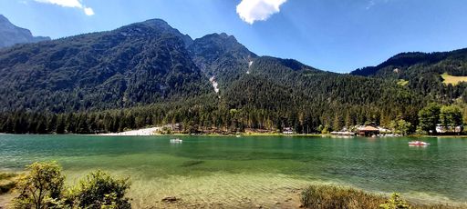 A panoramic shot of the beautiful nature scene with a clean and peaceful lake surrounded by pine trees and hills during the daytime