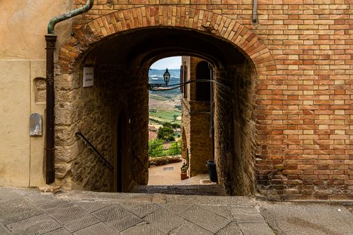 A narrow street through an arch between old stone houses of ancient, historical town in Volterra, Italy