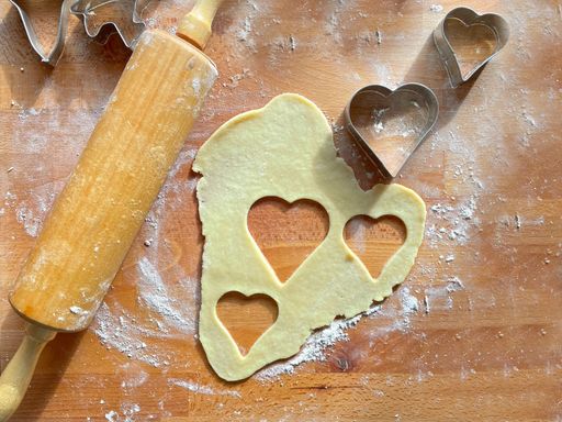 A closeup top view of three heart cuts on the dough and a wooden rolling pin on the table