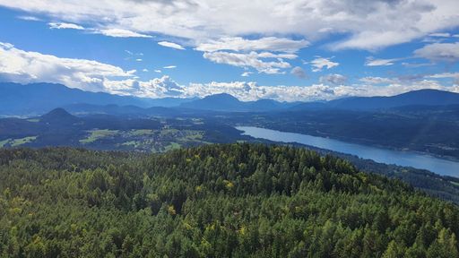 A landscape of a river surrounded by hills covered in greenery under a blue cloudy sky