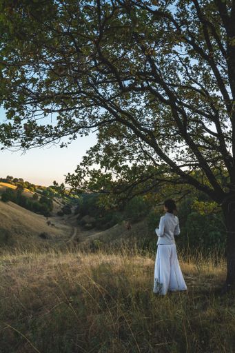 A vertical shot of a female in a white dress standing in on the dry grass in the mountains