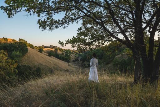 A female in a white dress admiring the horizon while standing in on the dry grass in the mountains