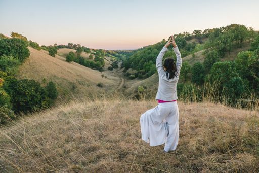 A female practicing yoga while standing on the dry grass in the mountains