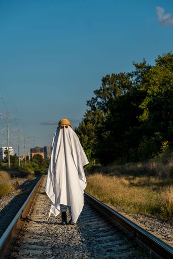 A vertical of a man covered with a white cloth looking like a ghost and walking between train rails