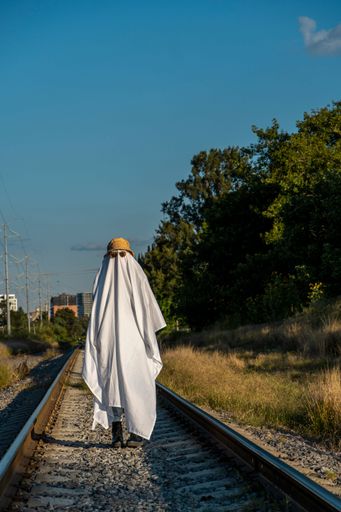 A vertical shot of the ghost wearing sunglasses and a bucket hat while walking along the railroad