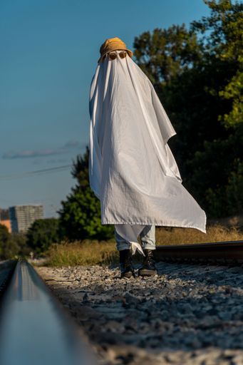 A man dressed as a ghost from a sheet and sunglasses crosses the road along the crosswalk