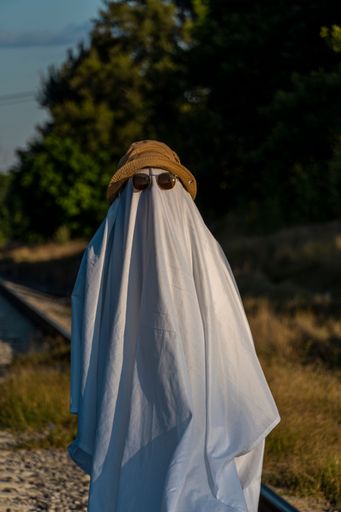 A man dressed as a ghost from a sheet and sunglasses crosses the road along the crosswalk