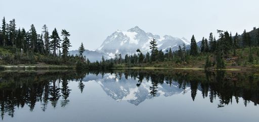 A breathtaking panoramic view of the snowy mount Shuksan in the background of a lake in the green forest