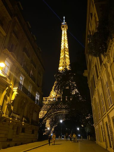 A vertical shot of the Eiffel Tower from the street view at night.