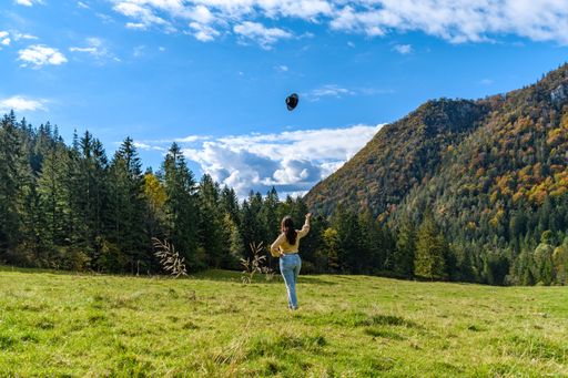 A back view of a Caucasian woman throwing her hat to the cloudy sky in a forest