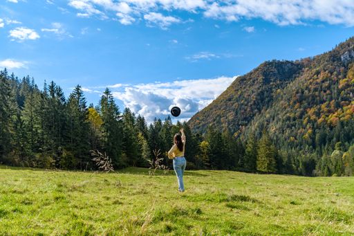 A back view of a Caucasian woman throwing her hat to the cloudy sky in a forest