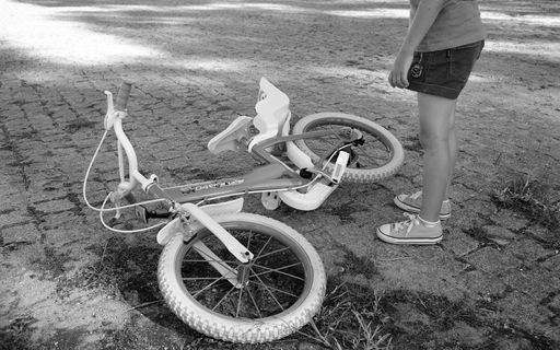 A young girl standing next to her small bicycle at a park