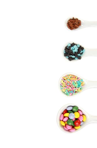 A vertical top view shot of candies in spoons on a white surface