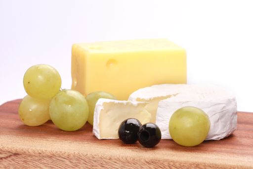 A closeup shot of two types of cheese and grapes on a chopping board isolated on a white background