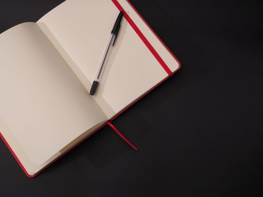 A closeup shot of an open and empty notebook for text with a pen isolated on dark background