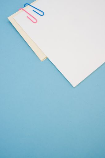A closeup shot of a blank paper with colorful paper clips on a blue background