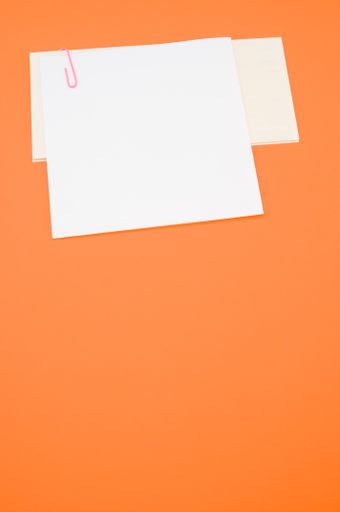 A closeup shot of a blank paper with a red paper clip on an orange surface