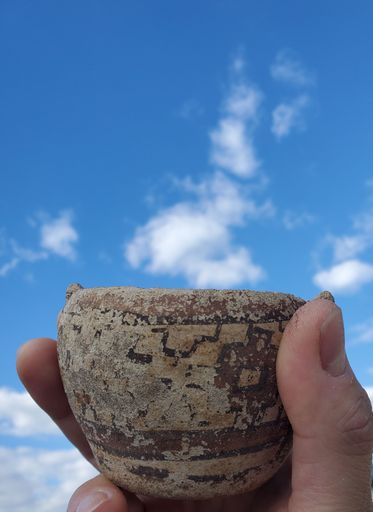 A close-up shot of a hand holding pre-columbian pottery cup with blue sky in the background