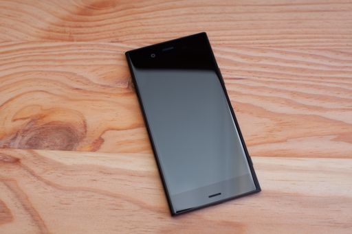 A top view of a black smartphone on a wooden table under the lights