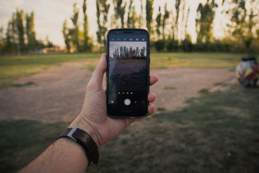 A closeup shot of a man's hand holding a phone and taking pictures of a beautiful summer landscape