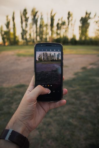 A closeup shot of a man's hand holding a phone and taking pictures of a beautiful summer landscape