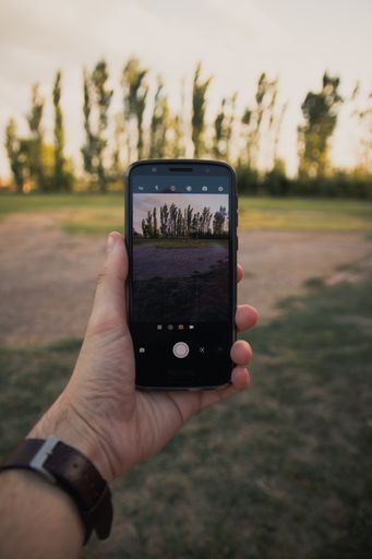 A closeup shot of a man's hand holding a smartphone and taking pictures of a beautiful summer landscape