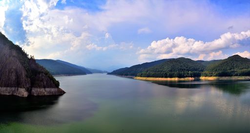 A panoramic view of a majestic cloudscape over a calm reflective Vidraru accumulation lake in Romania