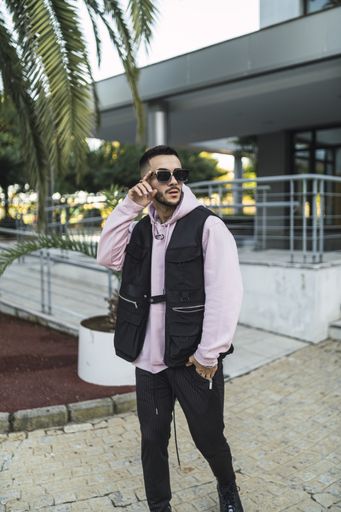 A vertical portrait of an attactive elegant man in a sporty outfit and stylish sunglasses posing against a modern building