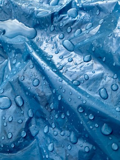 A closeup of the clean water droplets on a crumpled blue plastic surface