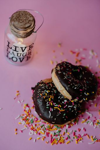 A closeup shot of delicious chocolate donuts with sprinkles and love notes on a pink background