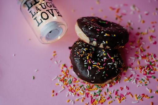 A closeup shot of delicious chocolate donuts with sprinkles and love notes on a pink background