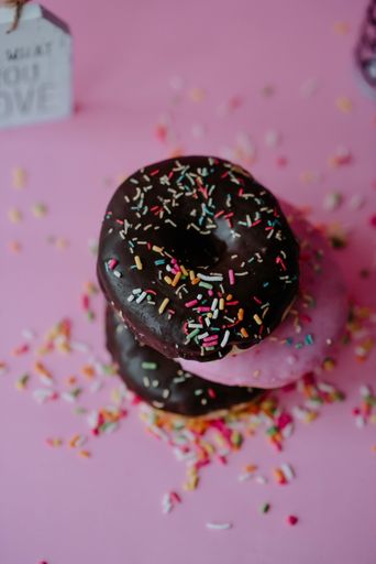 A closeup shot of delicious chocolate donuts with sprinkles and love notes on a pink background