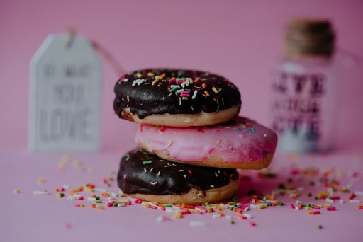A closeup shot of assorted chocolate donuts with sprinkles and love notes on a pink background