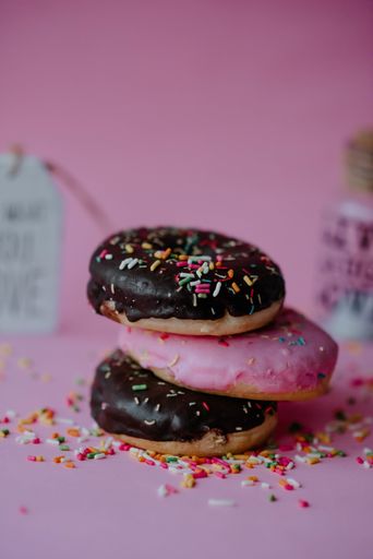A closeup shot of assorted chocolate donuts with sprinkles and love notes on a pink background