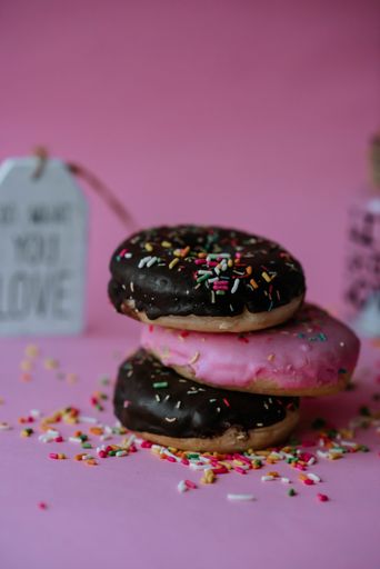 A closeup shot of assorted chocolate donuts with sprinkles and love notes on a pink background