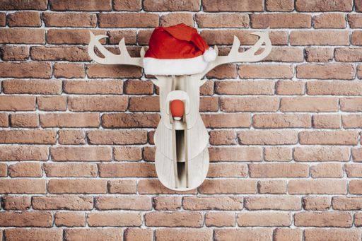 A wooden deer hanging on the wall with a Santa Claus hat and red nose