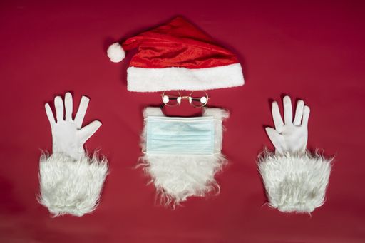 A high angle shot of Santa Clause hat and beard with a surgical mask on a red surface