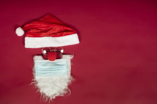 A high angle shot of Santa Clause hat and beard with a surgical mask on a red surface