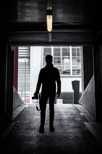 A vertical shot of a silhouette of a photographer standing inside a parking lot under a lamp