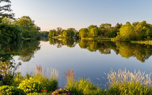 A breathtaking green scenery reflecting in the clear lake under the light blue sky