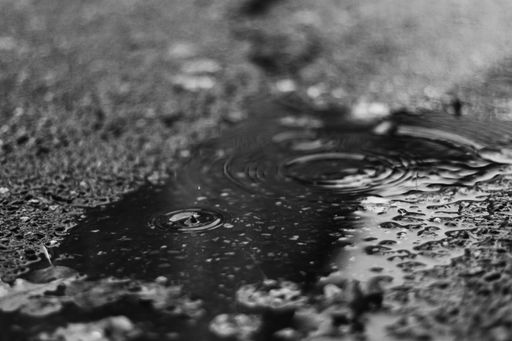 A greyscale shot of raindrops falling on the ground making plashes in the street