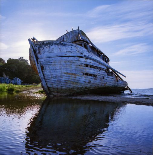 A low angle shot of an old rusty ship reflecting in the lake under the cloudy sky