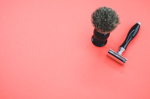 A closeup shot of a shaving brush and a razor on a red background