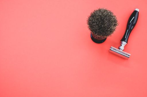 A closeup shot of a shaving brush and a razor on a red background