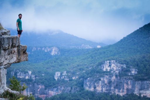 A scenic shot of a man standing on the edge of a cliff overlooking mountainous scenery