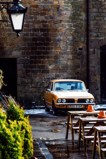 A vertical shot of an old-fashioned yellow car in front of an ancient brick wall