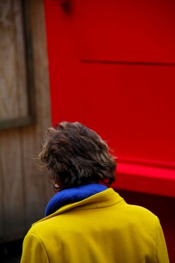 A vertical shot of a short-haired woman standing on the street in front of a red wall