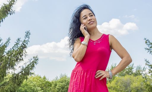 A young brunette girl stands against a blue summer sky and talks on the phone