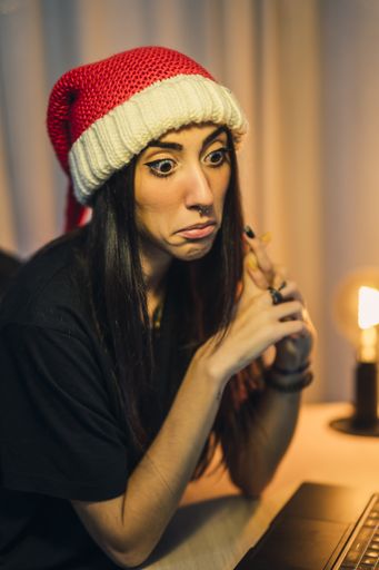 A vertical closeup portrait of a funny Caucasian woman with a questioned look wearing a knitted Santa hat